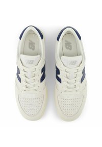 Valkoiset mokkanahkaiset lenkkarit, joissa on tummansinisiä yksityiskohtia, pyöreä kärki, rei'itetty päällinen ja valkoiset nauhat. Kengissä on kuvioitu pohja ja logomerkkki kielen kohdalla.