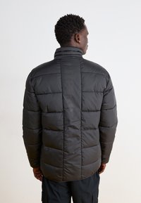 Giacca a puffo nera con colletto alto, caratterizzata da un design trapuntato e cuciture orizzontali. Il tessuto sembra liscio e lucido.