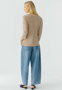 Bruin en crème gestreepte langelская shirt met een bootnek, gecombineerd met lichtblauwe wijde jeans en zwarte instap schoenen.