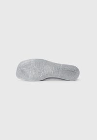 Semelle de chaussure en caoutchouc gris avec une surface texturée, présentant un devant lisse et un bord arrière légèrement courbé, avec des détails de marque en relief.