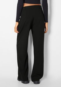Zwarte wijde broek met een gladde textuur, met een hoge taille en plooien, gecombineerd met een geribbelde lange mouw top en platte schoenen.
