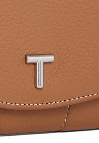 Borsa a tracolla in pelle color tan con superficie texture, caratterizzata da un accento in argento a forma di "T" e cuciture bianche lungo i bordi.