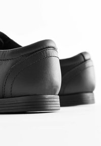 Chaussures en cuir noir avec une texture lisse, un design à profil bas, des talons ronds et des détails cousus le long des coutures.