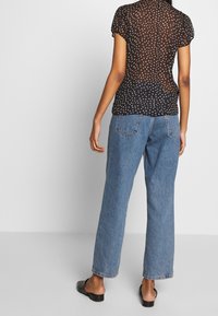Top trasparente nero con piccoli pois bianchi, maniche a sbuffo corte, abbinato a jeans dritti blu chiaro e sandali neri a ciabatta.