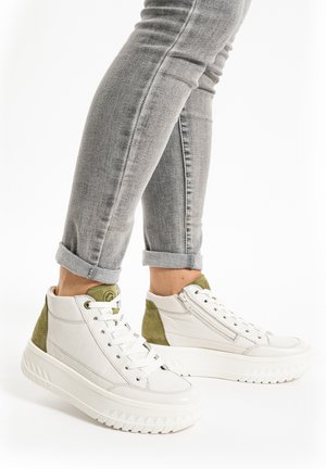 Person wearing light gray rolled-up jeans and white high-top sneakers with green suede back panels and thick soles.