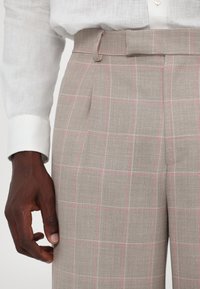 Pantaloni di lana beige con controlli a finestra in grigio chiaro e rosa, dotati di un frontale piatto, passanti per la cintura e una vestibilità su misura.