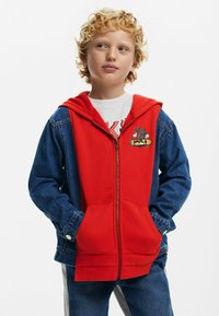 Red zip-up hoodie with a denim sleeve and hood, featuring a graphic design on the chest. Smooth texture, casual style, with pockets.