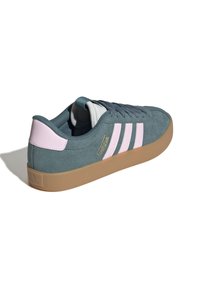 Gröna mockaskor från Adidas med rosa ränder och hälaccent, gummisula och snörning, visade från baksidan mot en vit bakgrund.
