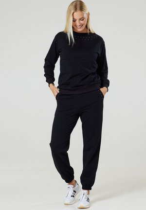 Black sweatshirt and joggers made of soft fabric; features stud accents on shoulders and pockets; elastic cuffs at ankles.