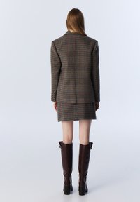 Blazer de cuadros en tonos marrones, verdes y naranjas combinado con una falda a juego. Botas de cuero marrón hasta la rodilla con tacones cuadrados.