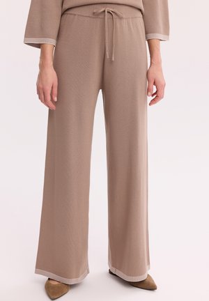 Beżowe szerokie dzianinowe spodnie z sznurkiem w pasie, noszone z dopasowanym topem i brązowymi, zamszowymi, spiczastymi butami.