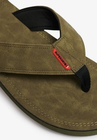 Chanclas de color verde oliva con parte superior de imitación de cuero texturizado, tira negra y etiqueta de logo roja. Incluye detalles de costura en contraste.