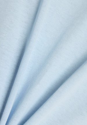 Pehmeä vaaleansininen kangas, jossa näkyy neulostekstuuri, taitettuna vinoon luoden lempeitä, virtaavia poimuja.