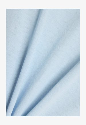 Pehmeä vaaleansininen kangas, jossa näkyy neulostekstuuri, taitettuna vinoon luoden lempeitä, virtaavia poimuja.