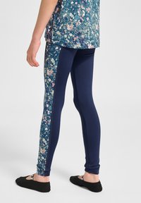 Leggings navy con un pannello laterale floreale in tonalità di rosa e blu. Tessuto morbido con un design aderente. Indossati con scarpe basse nere.