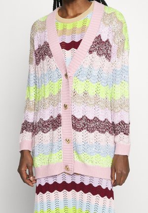 Meerkleurige gebreide cardigan met een gekartelde patroon, voorzien van een roze geribbeld kraag en hartvormige knopen, gedragen over een bijpassende jurk.