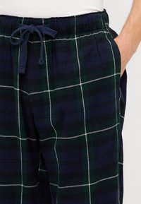 Námorné a zelené kockované pyžamové nohavice vyrobené z mäkkej tkaniny, s elastickým pásom a šnúrkou na stiahnutie, s bielymi akcentmi v vzore.