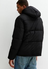 Zwarte pufferjack met een capuchon, met een geborduurd ontwerp, dikke vulling en lange mouwen, gecombineerd met blauwe spijkerbroek.