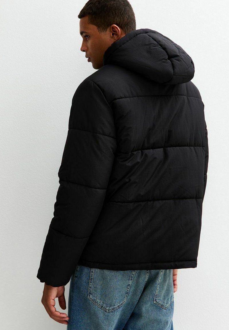 Chaqueta de plumas negra con capucha, diseño acolchado y textura ligeramente brillante. Combina con unos vaqueros de denim azul claro.
