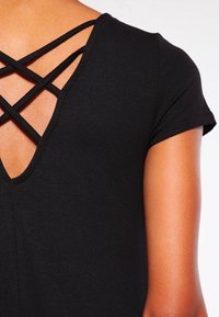 Haut noir avec un décolleté en V profond et un design de bretelles croisées dans le dos, avec des manches courtes et une texture lisse.