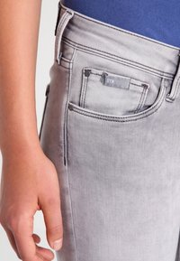 Vaqueros de mezclilla gris con un corte ajustado, que presentan costuras mínimas, cinco bolsillos y una pequeña etiqueta en la cinturilla. Textura suave.