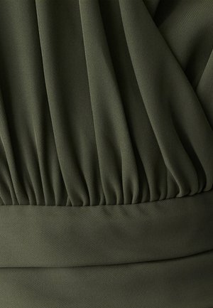 Olivgrüner Stoff mit texturierter Oberfläche, der oben Falten und unten ein glattes Band aufweist. Sanfte, fallende Optik durchgehend.