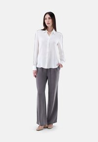 Lightweight white blouse with button closure, pointed collar, and black piping. Paired with flowy gray trousers and nude heels.