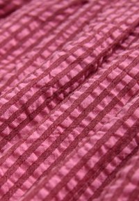 Pink stof med en ribbet struktur med vekslende mørkere og lysere stribede mønstre, der skaber et bølget udseende.