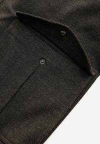 Țesătură neagră texturată cu un buzunar cu clapetă și butoane tip snap, evidențiind un design structurat și linii curate, minimalist.