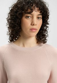 Jasnoróżowy sweter z dzianiny, okrągłym dekoltem i fakturowanym wzorem, z rękawami raglanowymi oraz miękkim, gładkim wykończeniem.