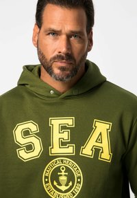 Felpa verde oliva con grandi lettere gialle "SEA" e un emblema nautico circolare sottostante con la scritta "NAUTICAL HERITAGE ESTABLISHED 1880."