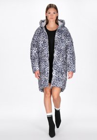 Gepolsterter Leopard-Print-Mantel mit Kapuze, in Grau- und Schwarztönen, mit einem zentralen Reißverschluss und Seitentaschen. Über einem schwarzen Kleid getragen.