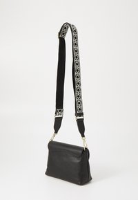 Borsa a spalla in pelle nera con una superficie testurizzata, dotata di una tracolla rimovibile a fantasia in bianco e nero, fissata da hardware dorato.