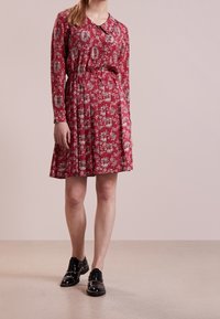 Czerwona kwiatowa sukienka z długimi rękawami, wiązanym w pasie i plisowanym dołem. Połączona z czarnymi butami z ćwiekami. Gładki materiał z szczegółowym nadrukiem.