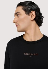 Czarny longsleeve z okrągłym dekoltem i nadrukiem na piersi "TRUSSARDI 1911" w kontrastowym kolorze. Gładka tekstura.