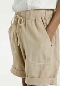 Beige shorts gemaakt van gestructureerde stof, met een tailleband met trekkoord, zijzakken en opgerolde zoom.