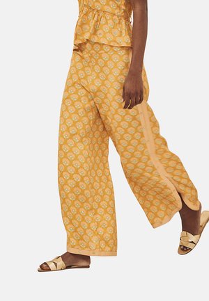 Pantalones amplios de rayas amarillas con un diseño floral, toques claros y un corte relajado, combinados con sandalias doradas.