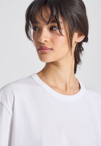 Tricou alb din bumbac, cu guler rotund și mâneci scurte, având o textură moale și o croială relaxată.