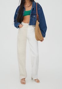 Chaqueta de mezclilla, top de canalé verde corto, pantalones de pierna ancha bicolor beige y blanco, bolsa de mimbre beige y sandalias blancas con tiras.