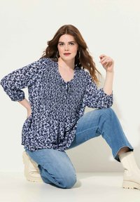 Blusa blu navy con stampe floreali, corpino arricciato, maniche 3/4 e scollatura con lacci, abbinata a jeans azzurri e stivali alla caviglia color crema.