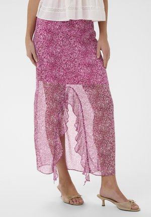 Priesvitná ružová midi sukňa so vzorom a volánikovým predným rozparkom, nosená s béžovými sandálmi na nízkom podpätku a bielym tričkom.