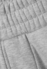 Gråt stof med en blød tekstur, der har en ribbet elastik i taljen og flade sømme. Materialet virker let og fleksibelt.