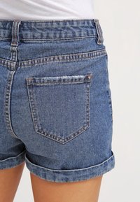 Denim shorts vaaleansinisinä, joissa on käännetty helma, kaksi takataskua koristeompeluilla ja vyötärö, jossa on vyölenkit.