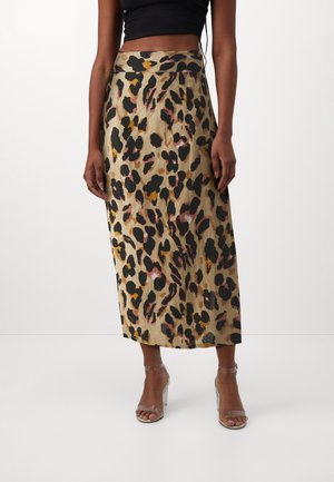 Kvinde iført et leopardmønstret nederdel med høj talje og midt på læggen, sort kort top og klare sandaletter med hæl.