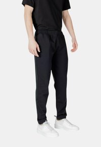 Schwarze Sporthosen mit schmalem Schnitt, elastischem Bund und Seitenstreifen. Hergestellt aus einem glatten, leichten Stoff. Kombiniert mit weißenSneakern.