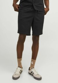 Shorts noirs en tissu texturé, longueur genoux, taille élastique avec cordon de serrage. Assortis à des baskets beiges et des chaussettes brun clair.