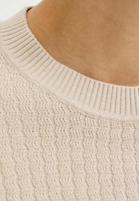 Beżowy sweter dzianinowy z teksturowanym wzorem w zygzak, z prążkowanym kołnierzykiem typu crew i miękkim materiałem o subtelnych odcieniach.