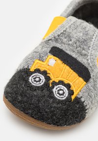 Grå hjemmesko med gult og sort broderet bulldozer design, udstyret med en brun gummisål og en velcrostrop for sikker pasform.