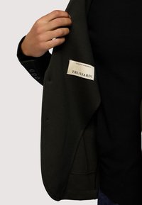 Trussardi jas met een khaki buitenkant, textiel met structuur en een zwarte voering. Voorzien van een merklabel en mouwboorden met vier knopen.