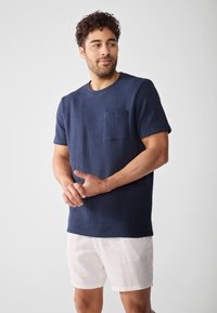 Tricou din bumbac texturat, de culoare albastru marin, cu mâneci scurte și un buzunar pe piept, asortat cu pantaloni scurți din in de culoare deschisă.